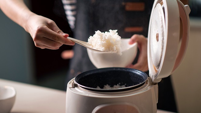 Person scooping white rice out of a steamer and into a bowl